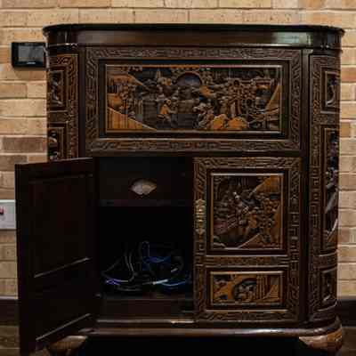 Opened cabinet of wood bar: The carved wooden Hong Kong bar features intricate designs on its panels and an open lower door.