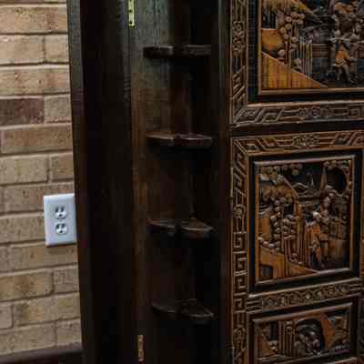 Opened cabinet of wood bar: The carved wooden Hong Kong bar features intricate panels and an open cabinet with shelves inside.