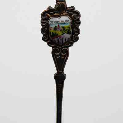 One of the collector's forks from Jerusalem.: Image of the silver collector's fork decorated with an enameled townscape on the handle. The top of the design reads "JERUSALEM." There is also silver details around the shield and handle of the spoon in swirls designs.