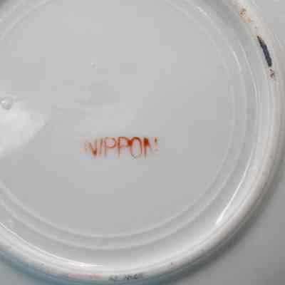 Bottom of the hand-painted Japanese porcelain saucer.: Up close image of the bottom of the white porcelain saucer. It is stamped in red ink with "NIPPON."