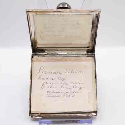 Inside of the square silver powder compact.: Image of the yellowed note found inside the square silver compact. The note reads "Persian Silver 'Powder Box' from: The sister of Shau Palvi Rhega to Jessie Jordan in Kuwait 1953" in black handwritten cursive.