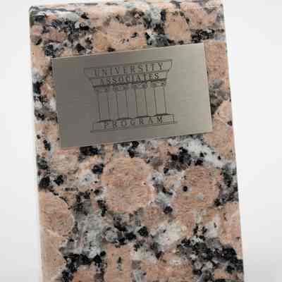 Pink granite polished bookends given to the Jordans by the University Associates Program at Texas A&M University.: Image of the left bookend with one silver plaque. The plaque at the top reads "UNIVERSITY ASSOCIATED PROGRAM" on a row of columns.