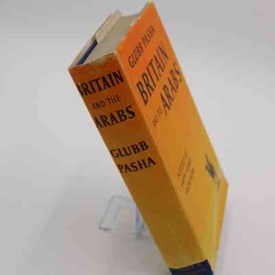 Spine of "Britain and the Arabs": Orange to yellow gradient reading "Britain and the Arabs; Glubb Pasha" in horizontal text. A small tear in the book jacket at the bottom shows the blue hard cover inside, with the publishers visible, "Hodder & Stoughton"