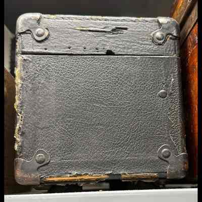 Black case, covered in textured material (leather or vinyl). Hinged lid, reinforced corners.