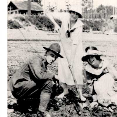 Alki, uniformed man and two women digging on beach.