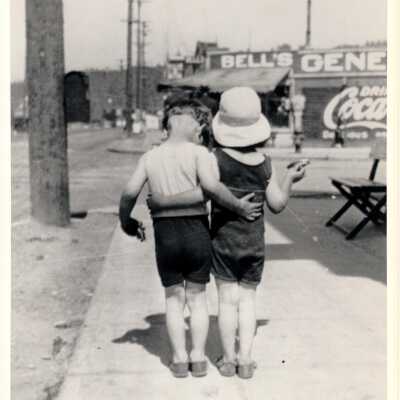 Rear view of two children with an arm around each other standing in front of Bell's General Store.