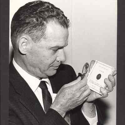 Photograph of E.A. Parker, a coin dealer from San Francisco, California, looking at $5.00 gold coin. Date unknown.