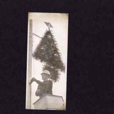 Photograph, Utility worker installs Christmas tree, date and location unknown.