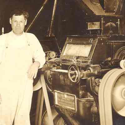 Photograph postcard of man standing next to a piece of equipment