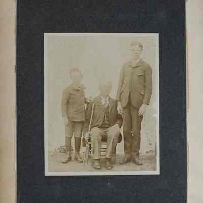 2016-024-012_img-003: Page 1 of photograph album 2016.024.012: Three unknown men, older is sitting with a cane and two younger men standing.