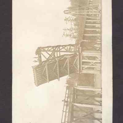 Photograph of drawbridge with two men standing on top and one man standing on bridge. Date unknown.