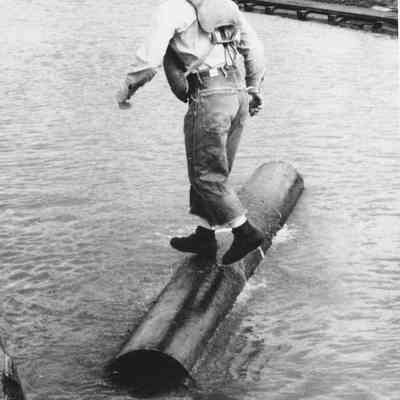 Photograph of unknown man standing on rolling log, date unknown
