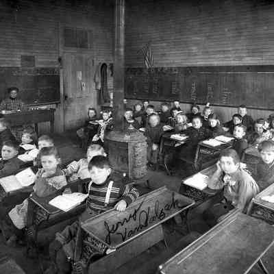 Photograph of interior early classroom with students at desks, date unknown.