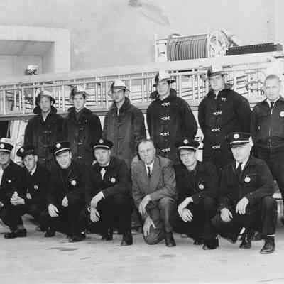 Photograph of firefighters in uniform posed in front of white fire truck, circa 1955