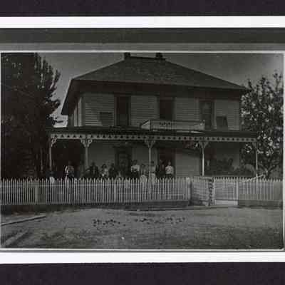 Photograph of an unknown group of eighteen people outside a house