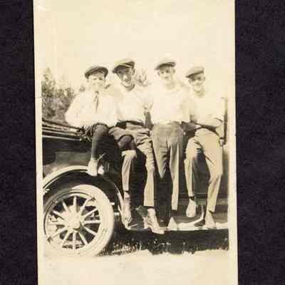 Photograph of 3 unknown men and an unknown boy sitting on the side of an open car