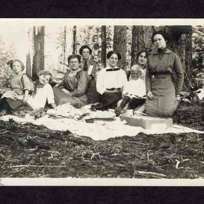 Photograph on postcard of 8 people on a blanket outside