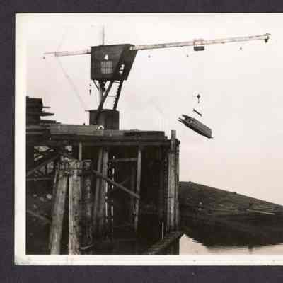 Photograph of a crane lifting lumber onto a barge, date unknown