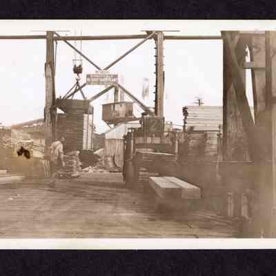 Photograph on postcard of a man with a load under an open craneway at Jones Lumber Company, Portland, Oregon, date unknown