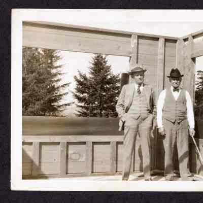 Photograph of two unknown men standing in frames building, date unknown