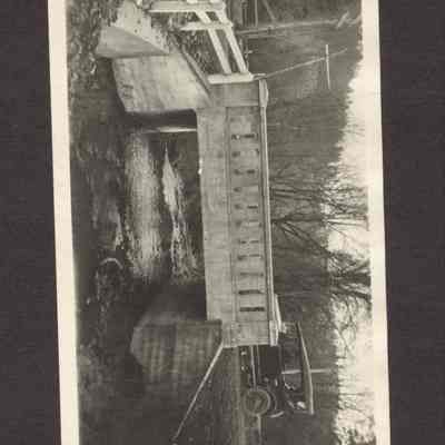Photograph of bridge over stream with a Ford Model T starting to cross over bridge. Date unknown.