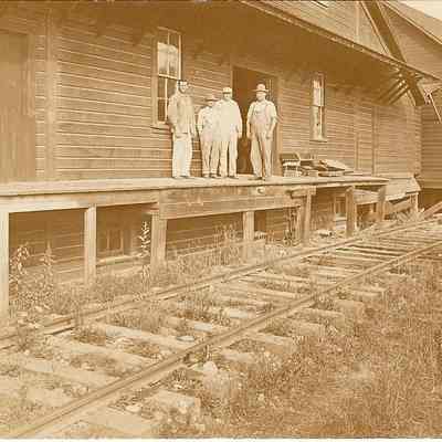 Photograph postcard of four unknown men standing on railroad platformStacking Wood