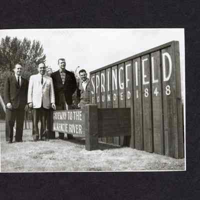 Photograph of 4 men standing by signs, "Springfield founded 1884" and "Gateway to the McKenzie River", undated