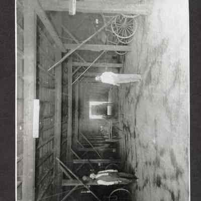 Photograph of two men standing in a wagon barn. Date unknown.