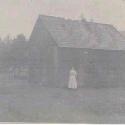 Photograph of Woman standing outside of Cabin, undated