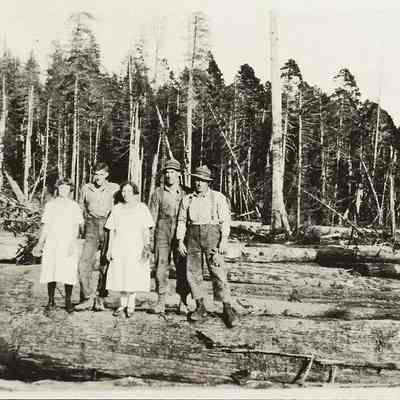 Photograph of three men and two women standing on a log
