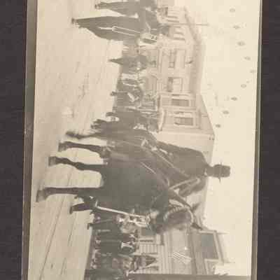 Photograph of a Post Card of a parade with a man on horseback and behind him is a marching band. Date unknown.
