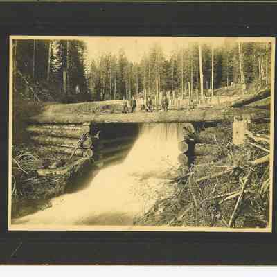 Photograph of Splash Pond with five men standing above the dam, date unknown