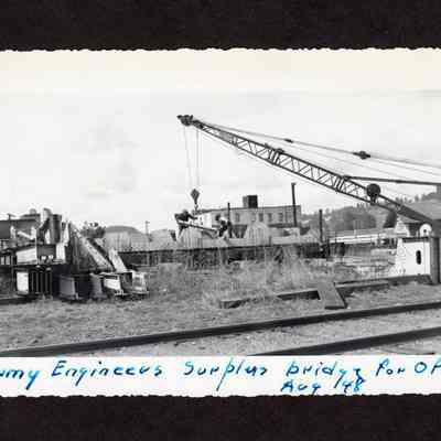 Photograph of two unknown men loading supplies onto a train car from a crane, 1948