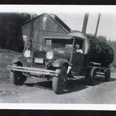 Photograph of a man driving a logging truck with a log in the bed, Mabel, Oregon
