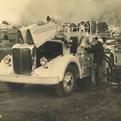 Photograph of white fire truck at hydrant, connecting hoses to truck, Mill fire, 1949