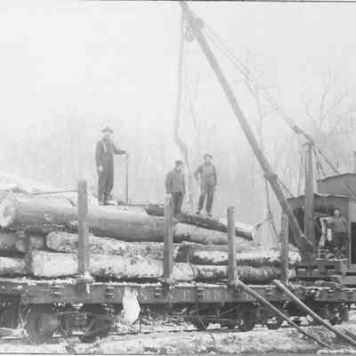 Photograph of four men loading logs on a train
