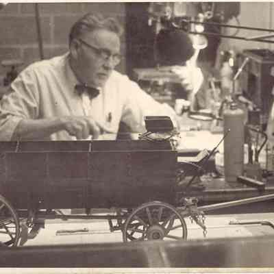 Photograph of unknown man with mini wagon and stagecoach in front of him