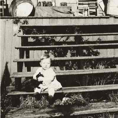 Photograph of small child holding a black cat on the steps of a house, Wendling, Oregon