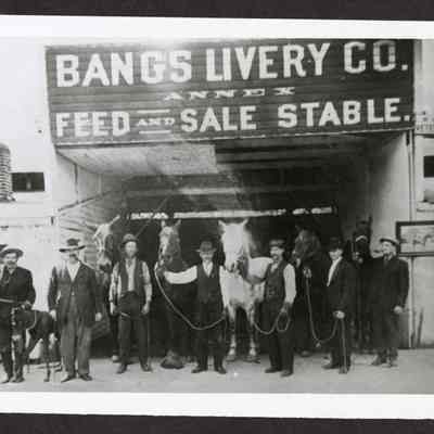 Photograph of eight men and seven horses at Bangs Livery Co. Annex Feed and Sale Stable