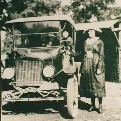 Photograph of unknown women standing beside an early car