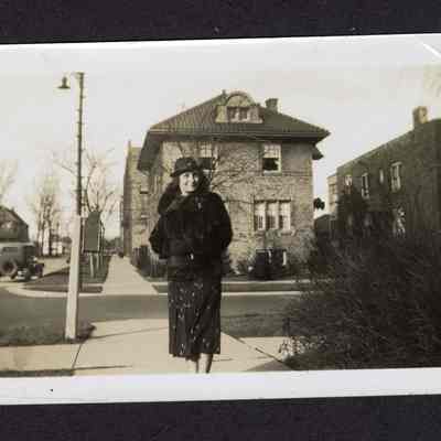 Photograph of a woman posing in front of brick houses, undated
