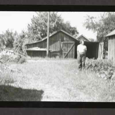 Photograph of a Wooden frame barn with lady, date unknown