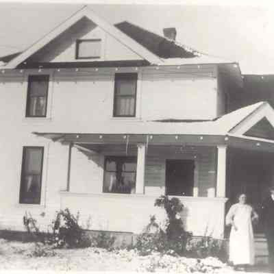 Photograph of an unknown women and man standing in front of a house