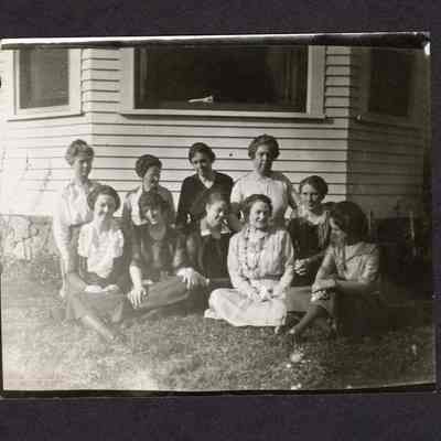 Photograph of 10 women sitting on grass in front of house