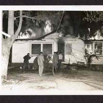 Photograph of unidentified people with hoses putting at a fire at a house