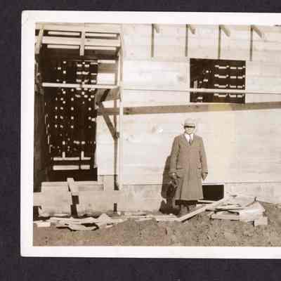 Photograph of unknown man standing outside of home under construction, date unknown