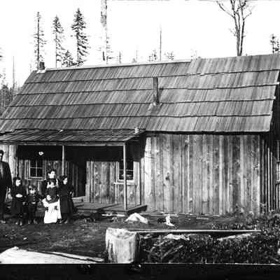 Photograph of Wooden House with Family of 6 in Front