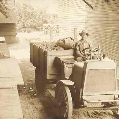Photograph postcard of a man in an early truck with sacks in trunk