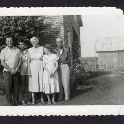 Photograph of five people in front of a brick house, circa 1950