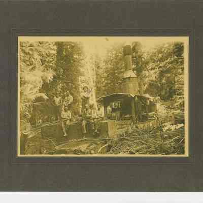 Photograph of six unidentified men on front of square cut log on the Steam Donkey, date unknown